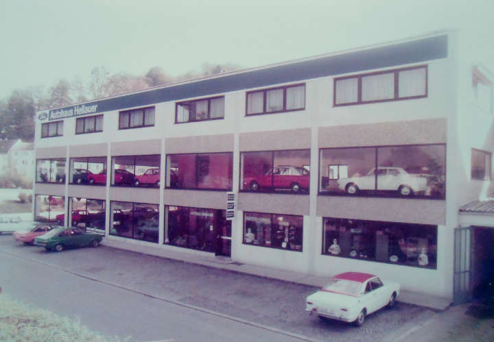 Historisches Foto eines mehrstöckigen Autohauses mit Fahrzeugen in den Schaufenstern.