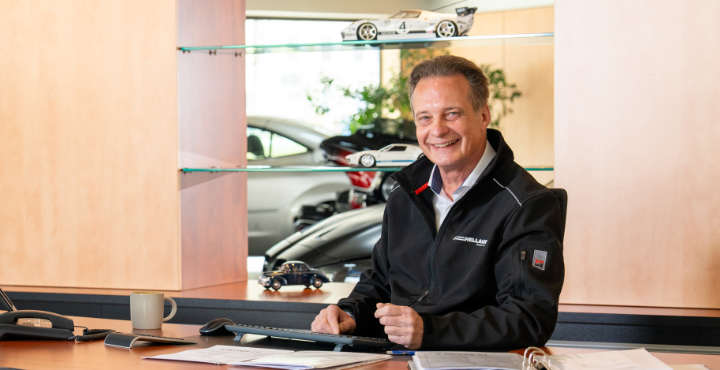 Peter Hellauer sitzt lächelnd an einem Schreibtisch im Autohaus.